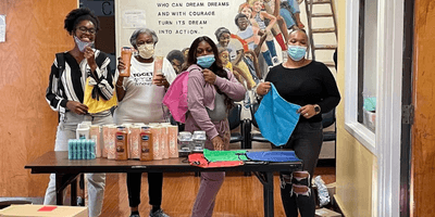 Recipents and leaders from Cambridge Community Center hold up Care Packs full of hygiene products and other essentials.