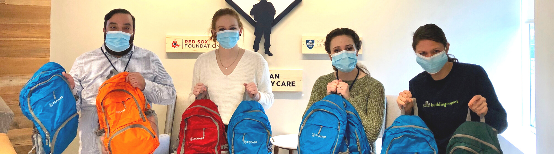 Nonprofit partners at Home Base and a Building Impact team member hold up Welcome Bags for Veterans.