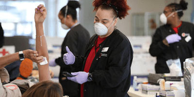 Red Cross employee speaks with patient getting her blood drawn to donate.