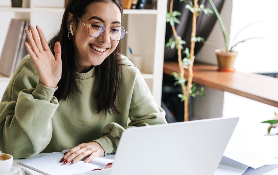 A young woman waves hello as she logs into a virtual professional development session.