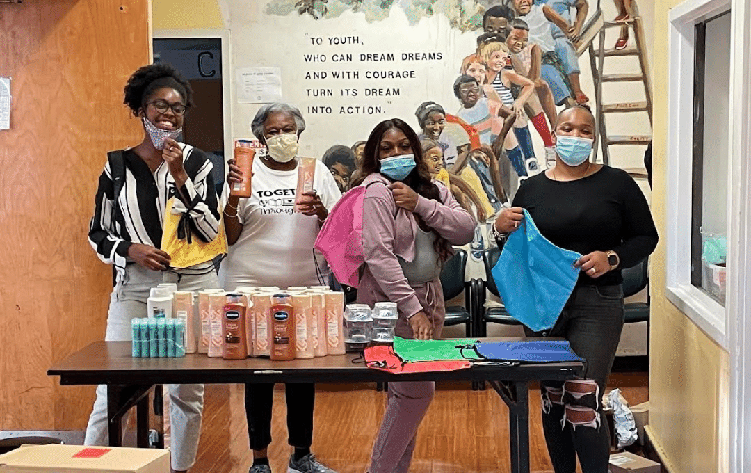 Nonprofit representatives from Cambridge Community Center hold up Bare Necessities Bundles containing hygiene products and other essentials.